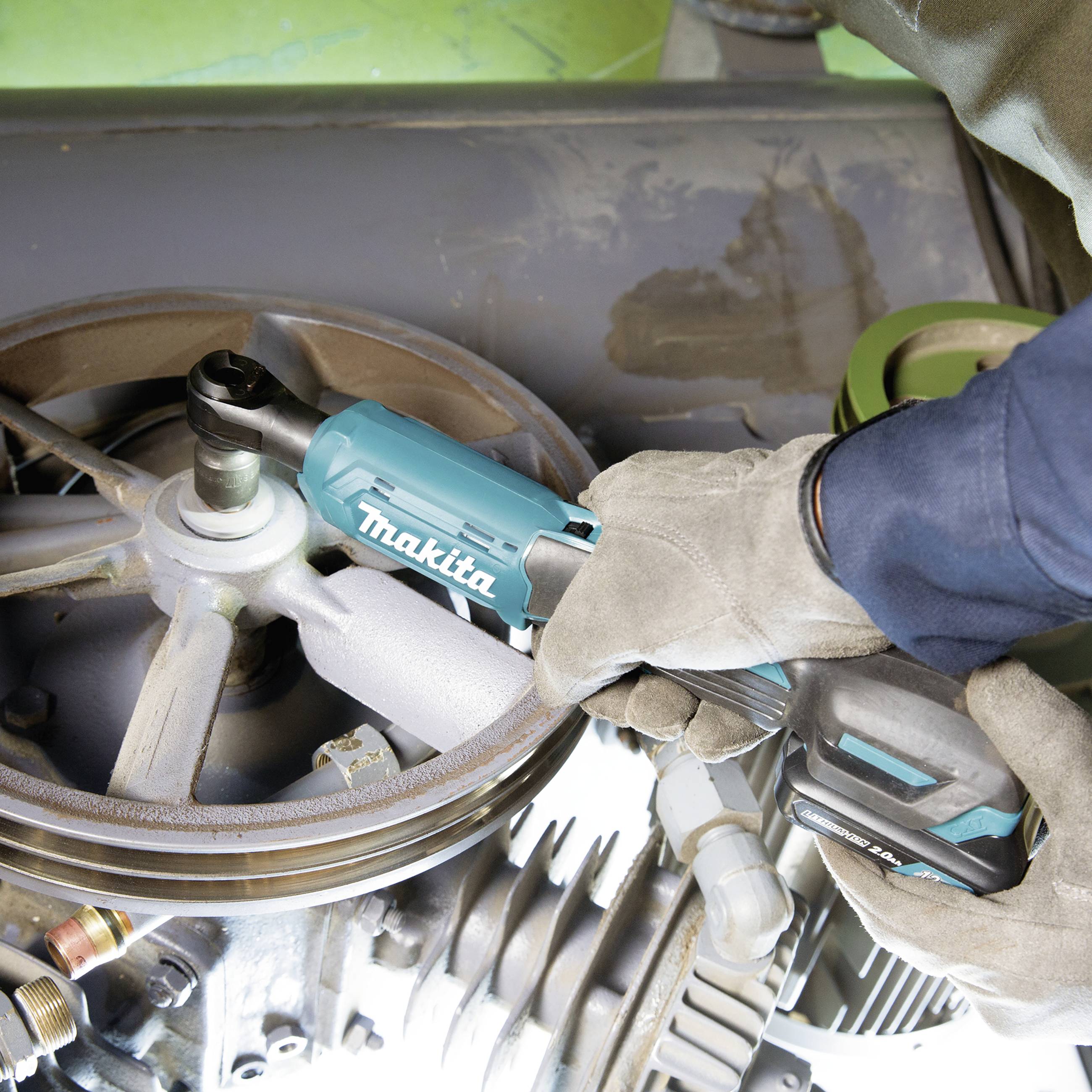 En mekaniker med handskar använder ett elektriskt verktyg från Makita för att arbeta på en stor metallmaskin.