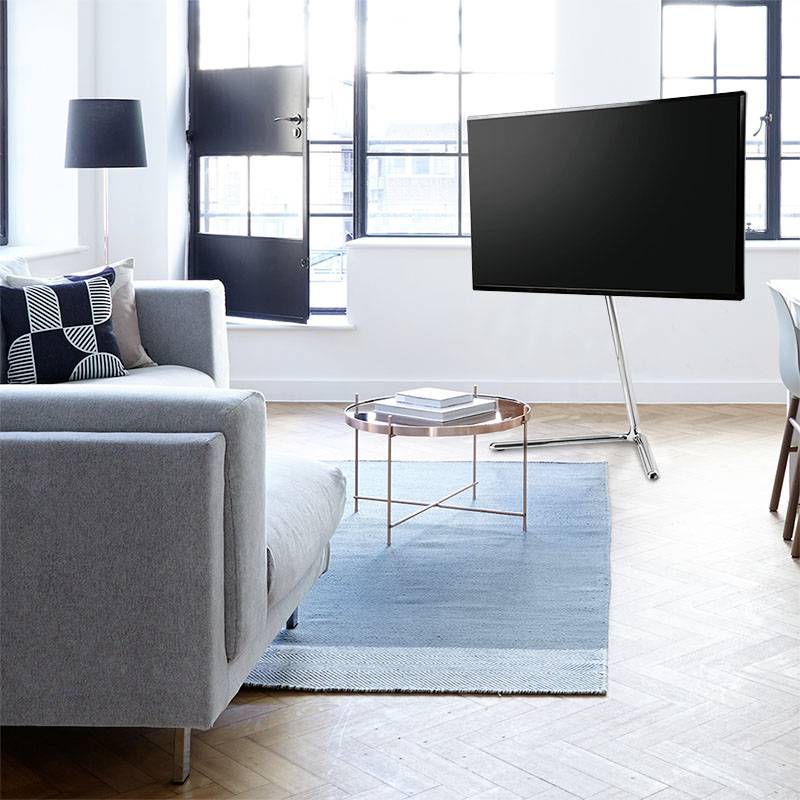 Ett modernt vardagsrum med en grå soffa, ett runt glasbord på en blå matta och en stor platt-TV.