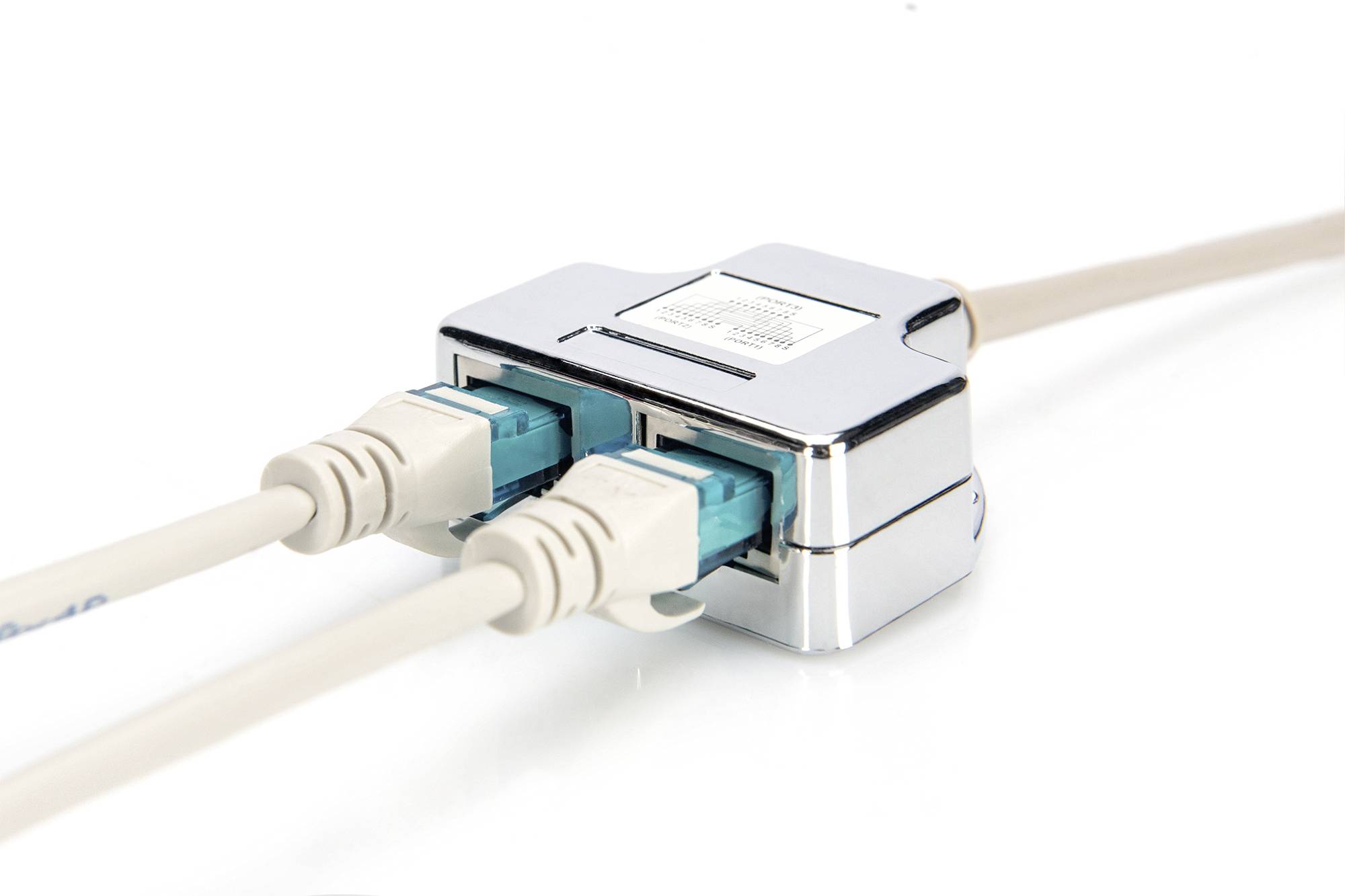 Två beige Ethernet-kablar är anslutna till en silverfärgad nätverksswitch som ligger på en vit yta.