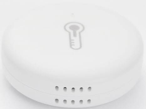 En vit, rund temperatursensor med en termometersymbol på. Små hål på sidan tyder på ventilation.
