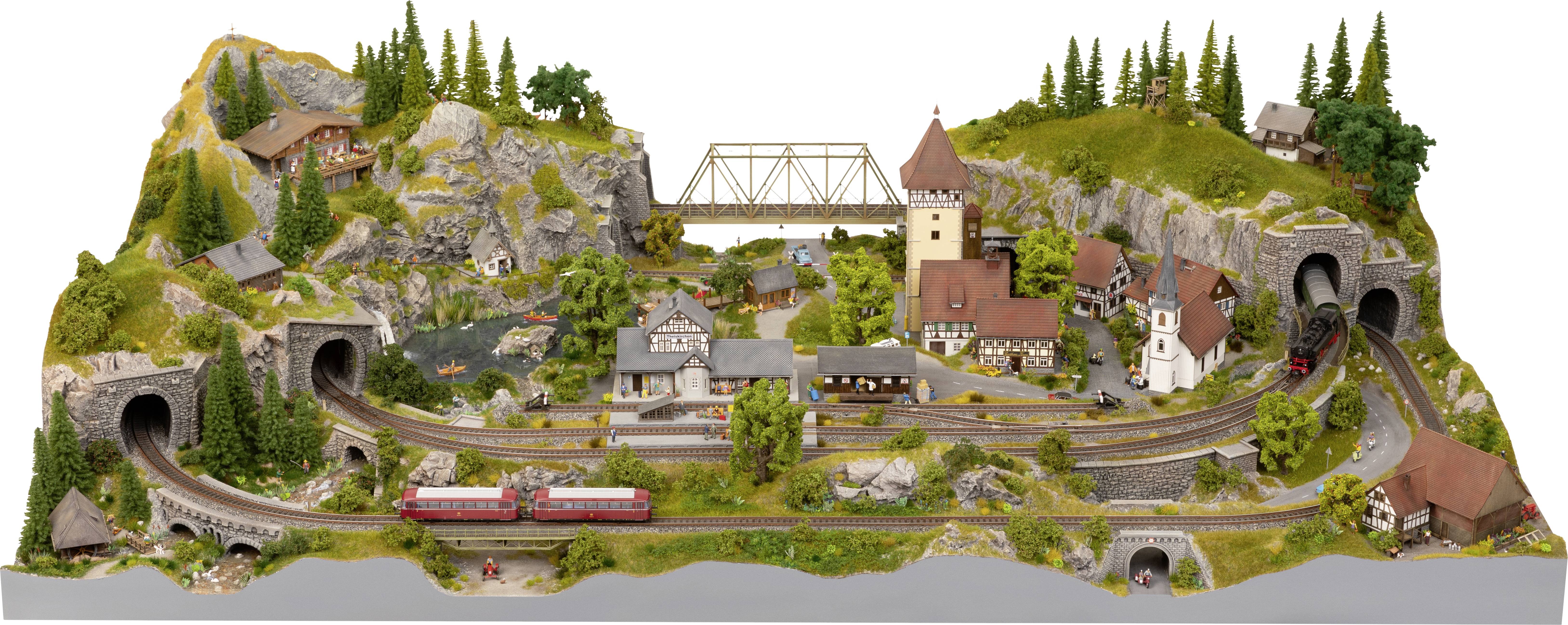 Modelljärnvägslandskap med ett tåg som färdas genom ett bergigt landskap med tunnlar, broar och en by med en kyrka.