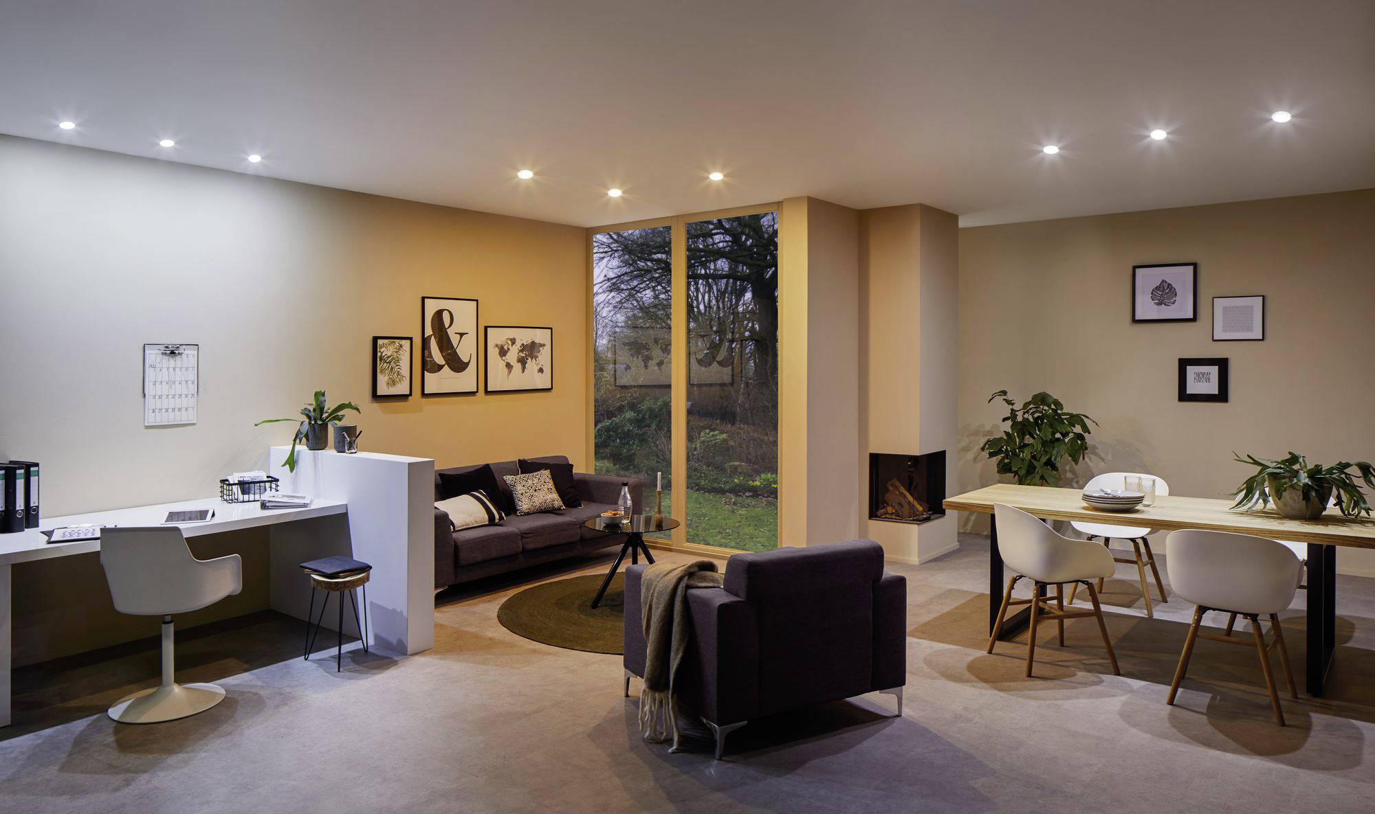 Öppen planlösning med modern arbetsplats, soffa, soffbord och matbord. Stora fönster erbjuder utsikt över trädgården.