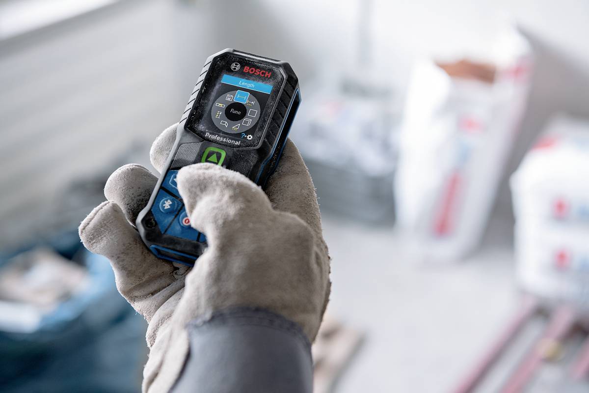En handskklädd hand håller ett avståndsmätningsinstrument med en digital display, perfekt för byggnads- eller renoveringsarbeten.