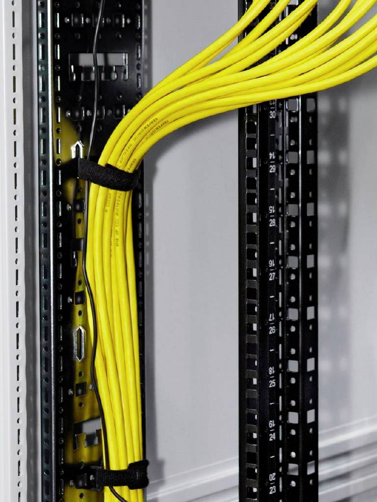 Gula kablar i ett serverrack, prydligt fästa med kabelbindare, löper vertikalt. Anordningen ser organiserad och strukturerad ut.