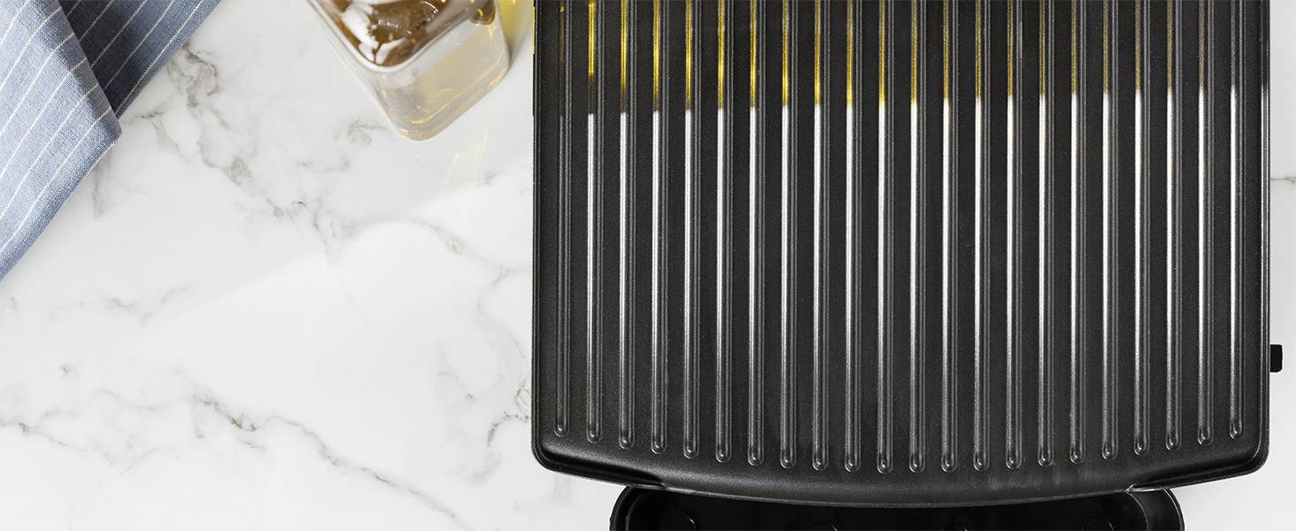 En svart grillplatta på en marmoryta med en blå kökshandduk och ett glas olja bredvid.