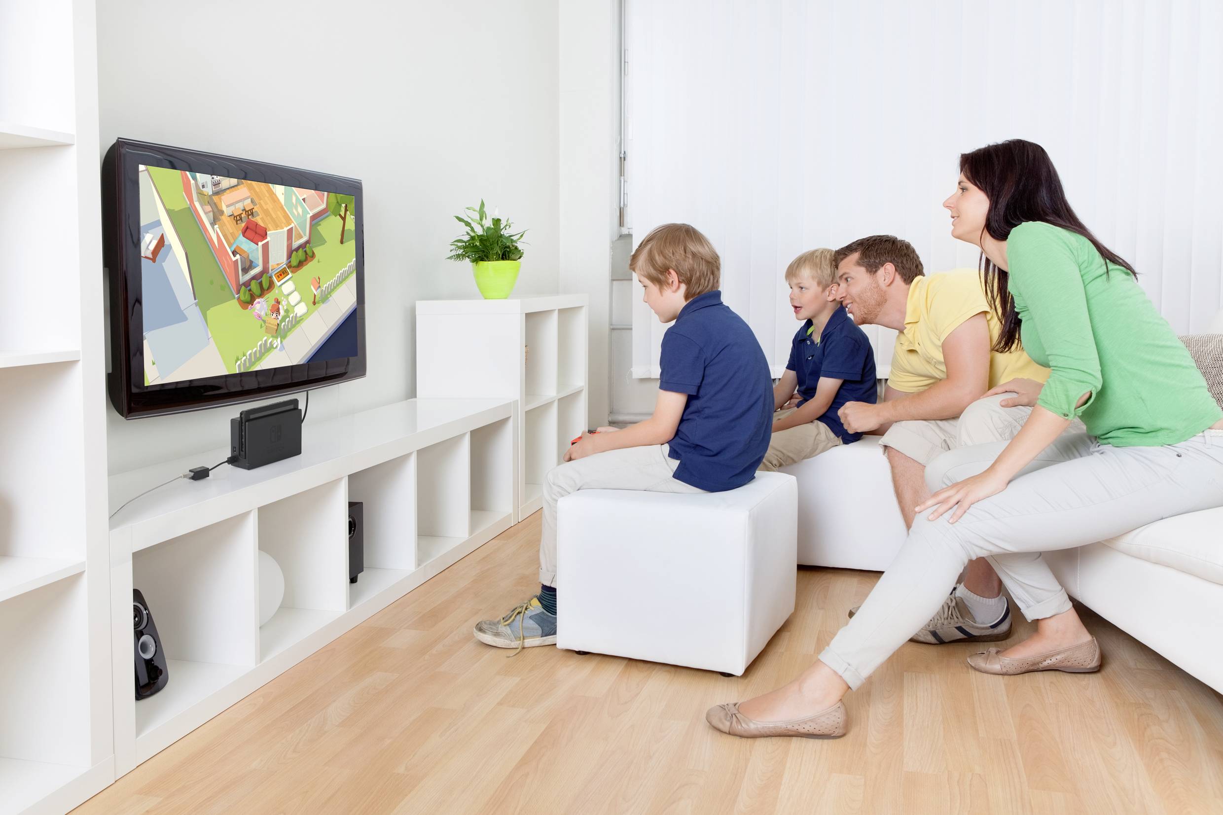 En familj sitter i vardagsrummet och tittar på tecknade serier på TV. Tre barn och en vuxen betraktar skärmen fokuserat.