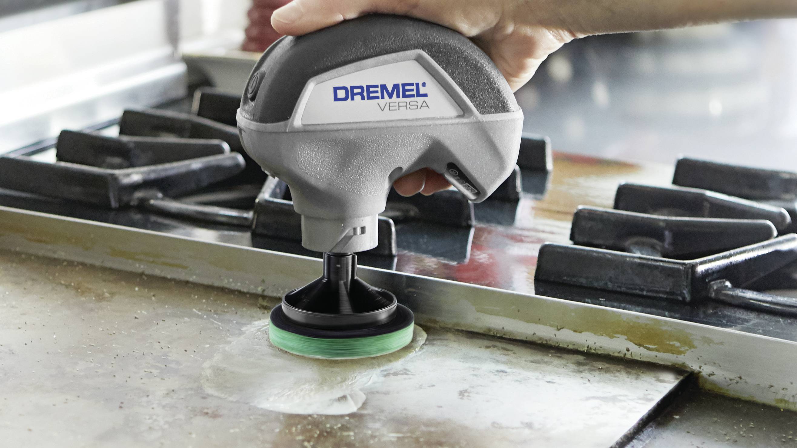 En hand använder en Dremel Versa rengöringsapparat för att rengöra en smutsig spishäll på ett kök.