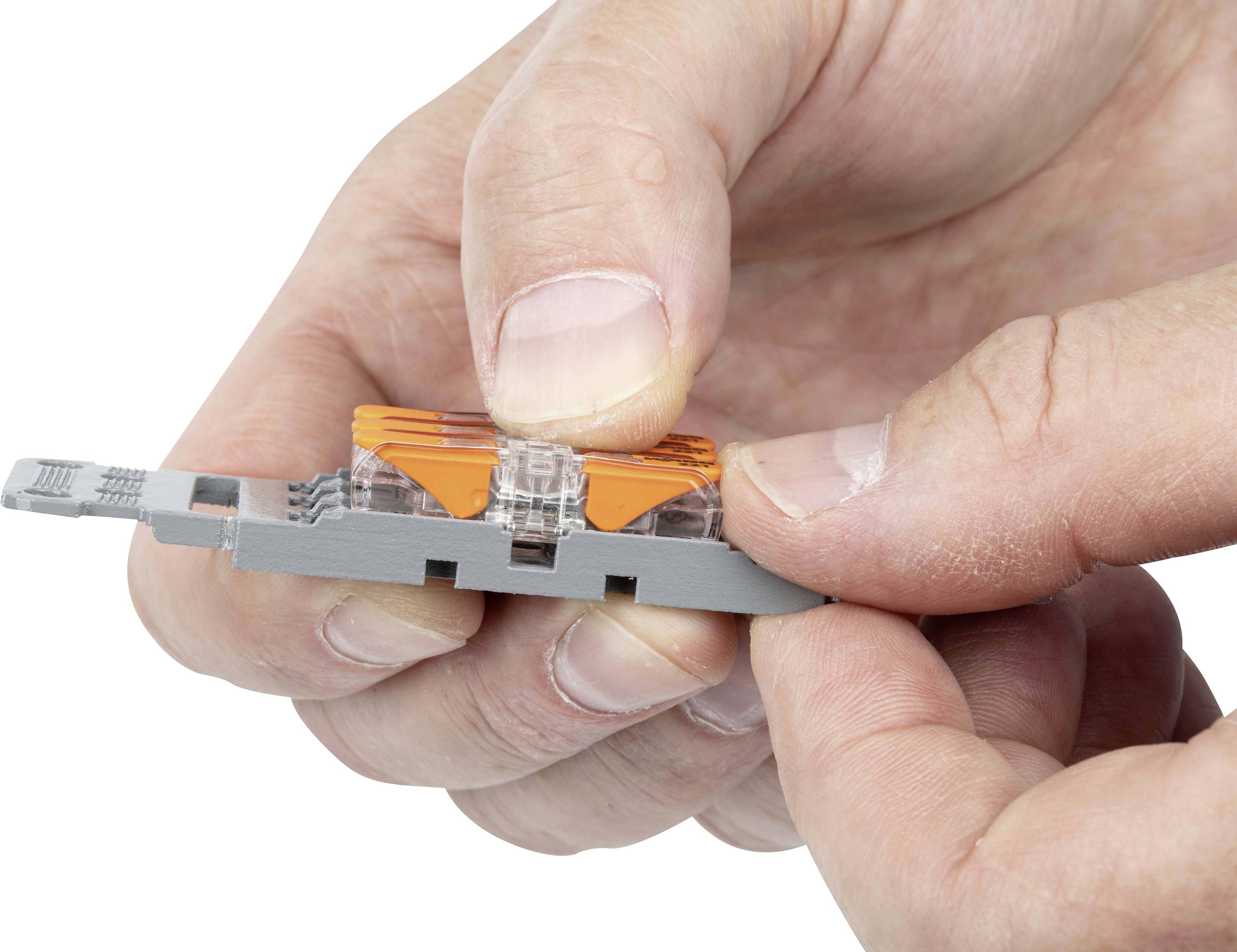 En person håller en grå strömbrytare med ett transparent och orangefärgat element mellan fingrarna.