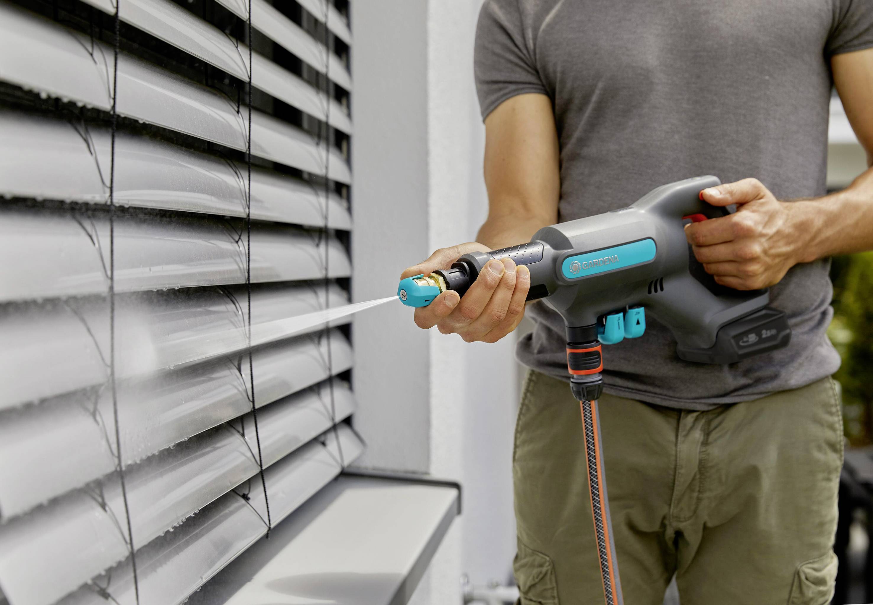 En person rengör persiennerna på ett hus med en elektrisk trädgårdsspruta och sprutar vatten på dammet.