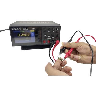 En person mäter resistansen hos en grön resistanskomponent med ett digitalt multimeter som visar 0,9962 kΩ.