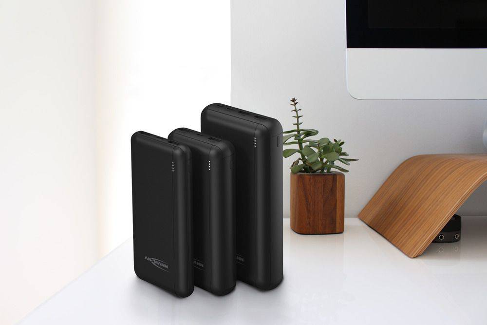 Tre svarta powerbanks i olika storlekar står på ett vitt bord bredvid en liten grön kruka.