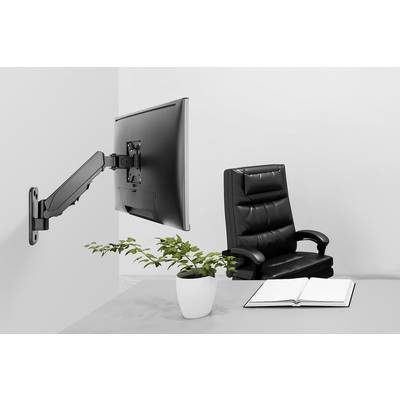 Ett tomt skrivbord med en öppen bok och en krukväxt. En monitor är monterad på en svängbar arm på väggen. En svart kontorsstol står bakom.