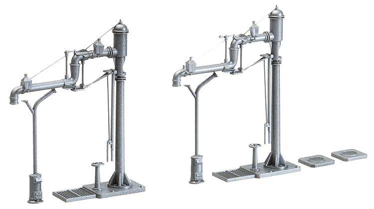 Två silvermetallfärgade vattenkranar för ånglok i modelskala, med detaljerade rör och basplattor, avsedda för tågförsörjning.