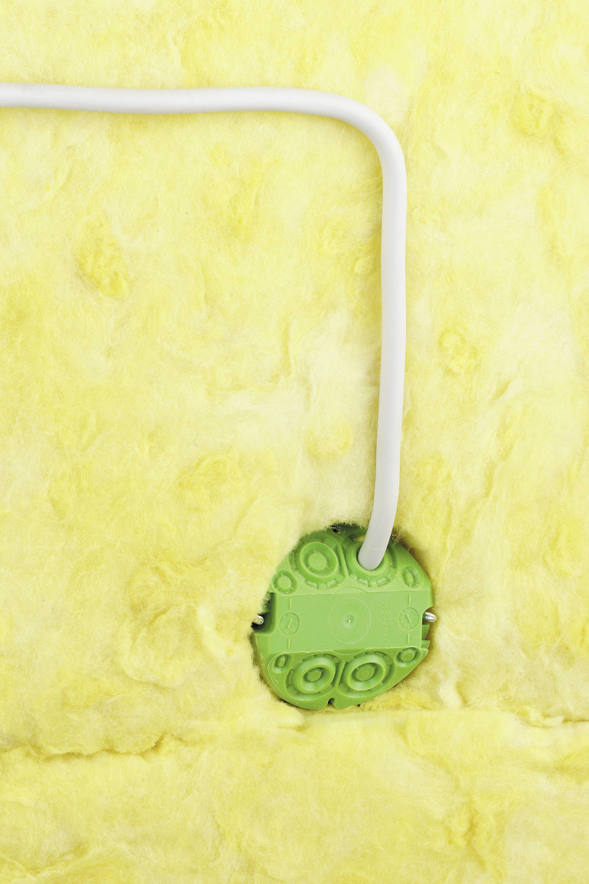 En grön vägguttag är inbyggt i gul isoleringsull, med en vit kabel som leder till den.