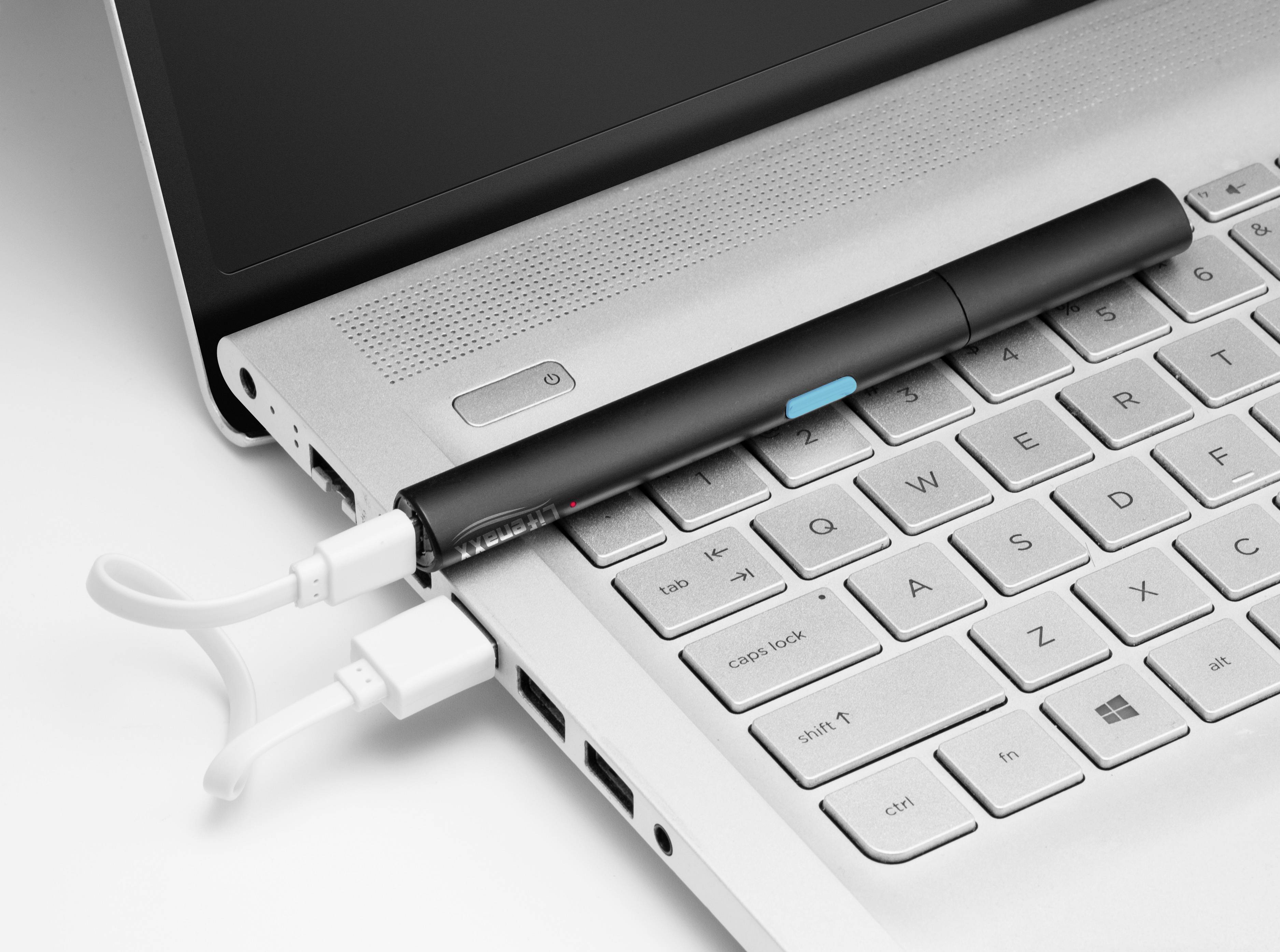En svart penna ligger på en laptops tangentbord. Ett USB-kabel är anslutet bredvid pennan, vilket tyder på teknologisk funktionalitet.