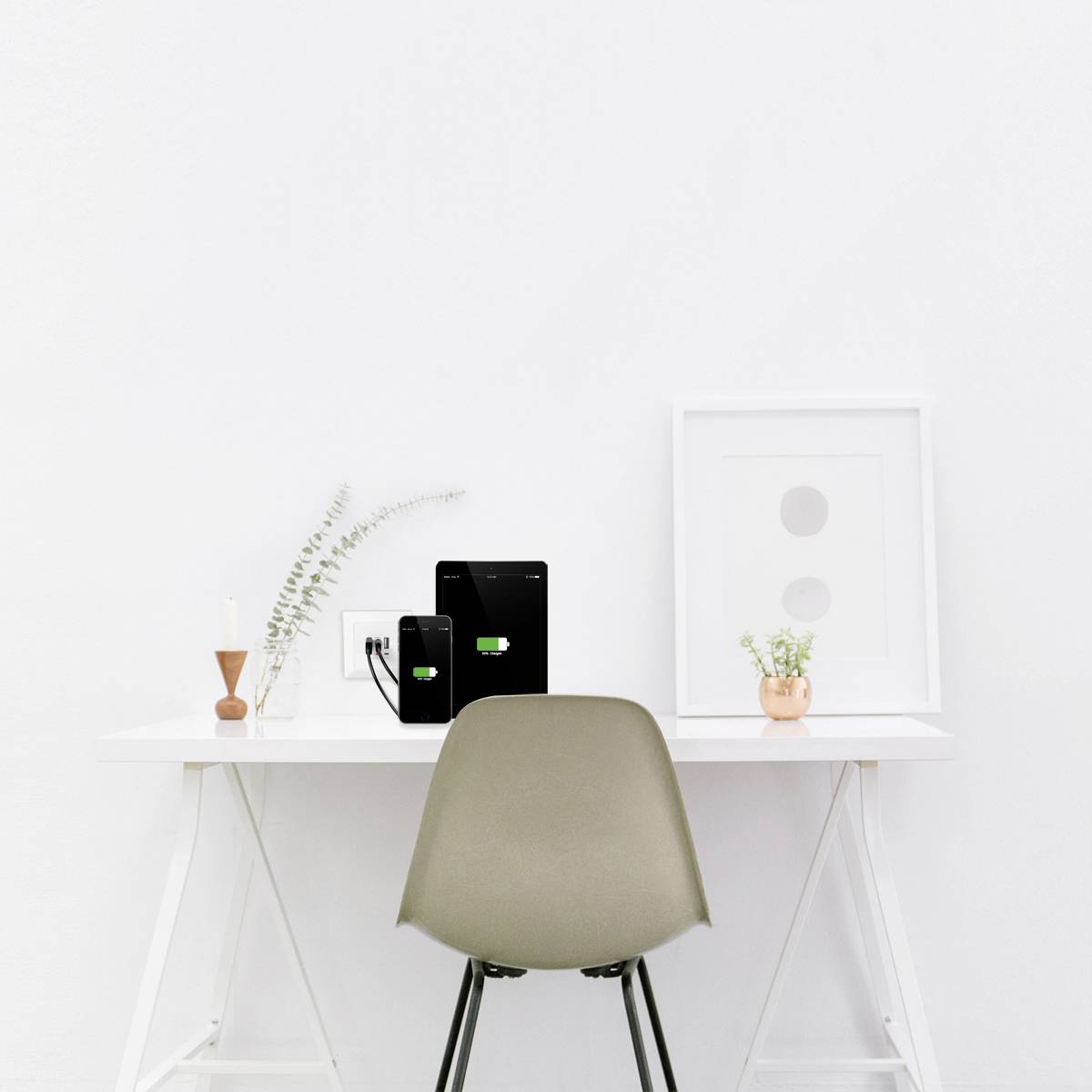 En minimalistisk arbetsplats med vitt skrivbord, brun stol, två uppladdade surfplattor, ljus, vas och inramat foto.
