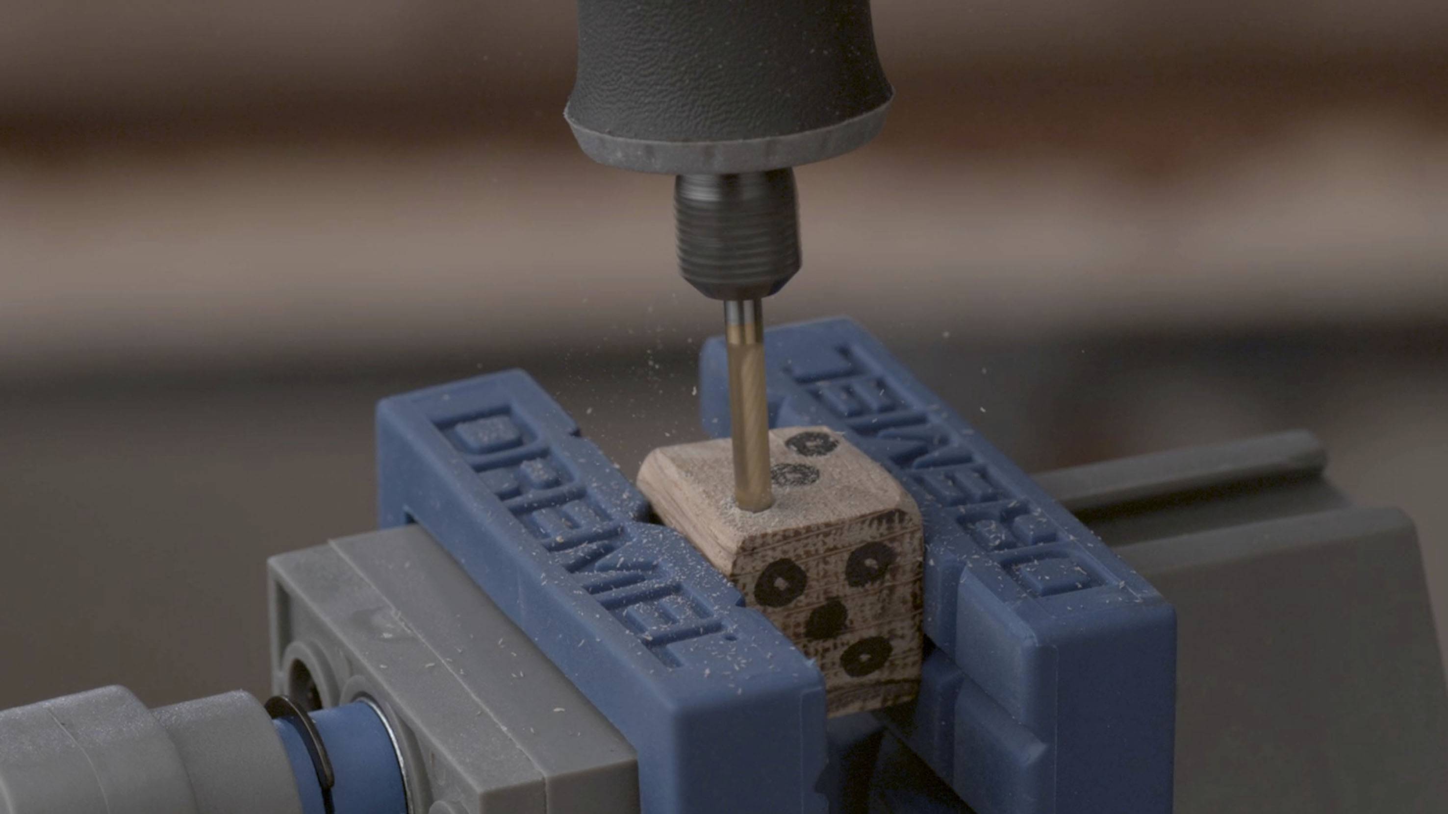 En fräsmaskin bearbetar en liten träblock som är fastklämd i ett skruvstäd. Träspån flyger omkring.