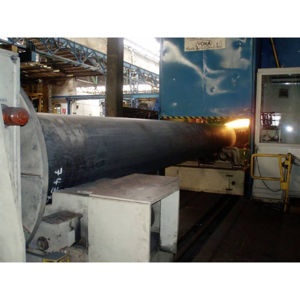 En stor metallcylinder bearbetas vid slutet av en hydraulpress. En orangegul glöd visar uppvärmningsprocessen.