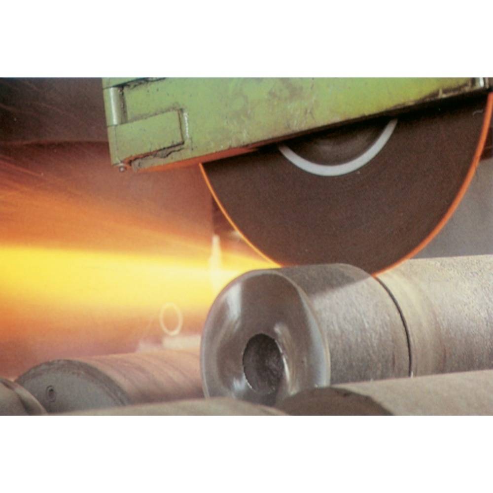 En stor roterande metallskärare skär genom tjocka metallrör i en industriell miljö, medan gnistor flyger.