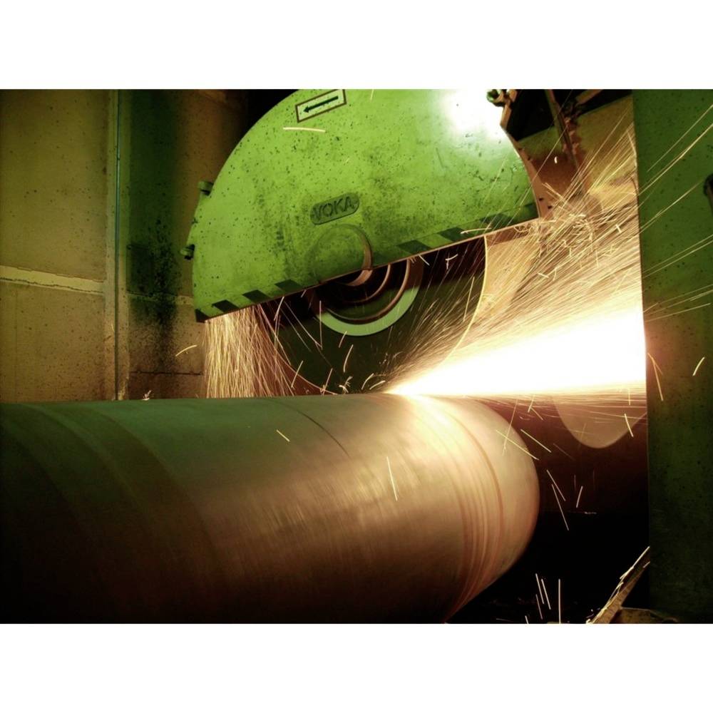 En slipmaskin bearbetar ett stort metallstycke, gnistor flyger. Industriell miljö som visar precisionsbearbetning av metall.