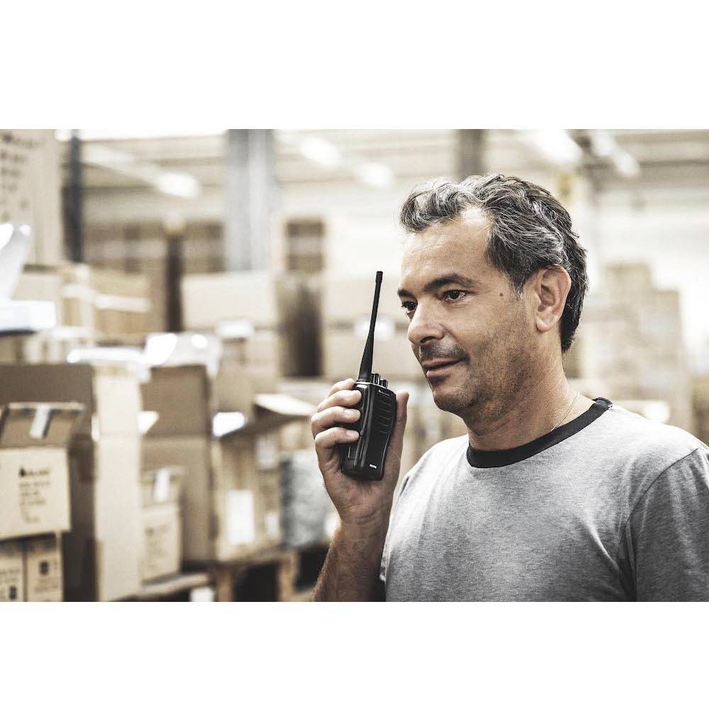 En man i ett lager pratar i en walkie-talkie. Han står mellan hyllor med lådor staplade på pallar.