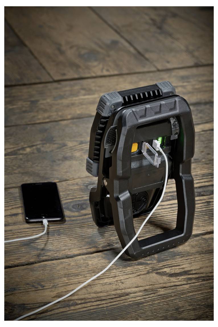 Bärbar elvärmefläkt med en telefonladdare bredvid den på ett trägolv, ansluten med en vit kabel.