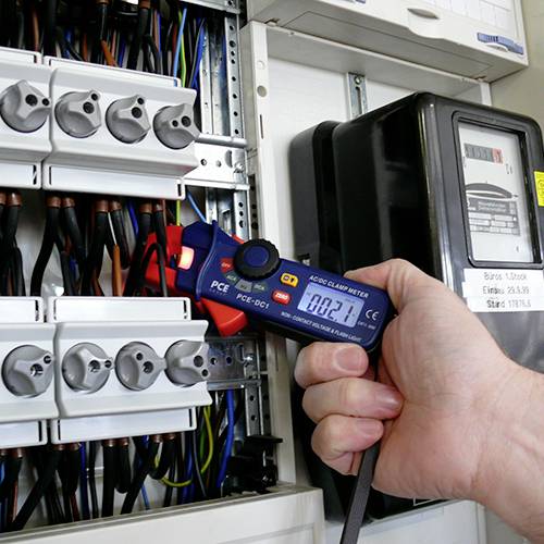 En hand håller ett digitalt mätinstrument som mäter strömmen i en elcentral.