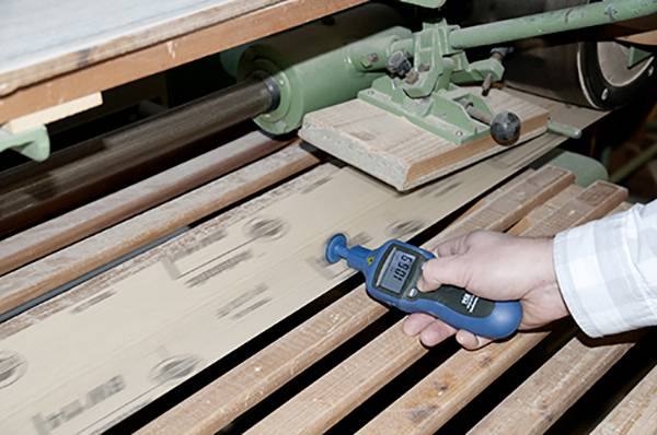 En person mäter hastigheten på ett roterande transportband med en blå handenhet som visar '10.6'.