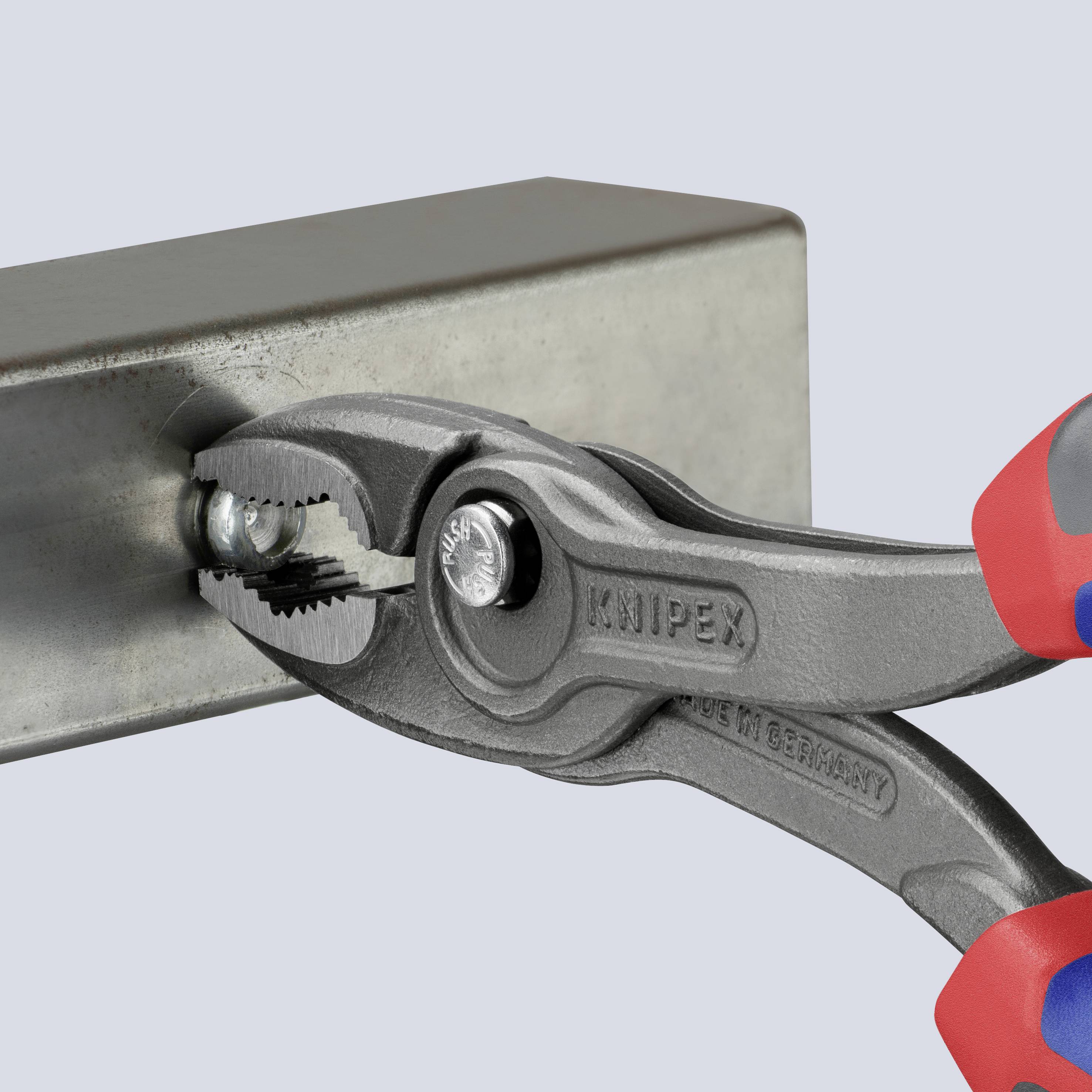 En tång håller fast en metallskena. Tångens märke 'Knipex' är synligt. En del av en hand i en röd handske håller tången.