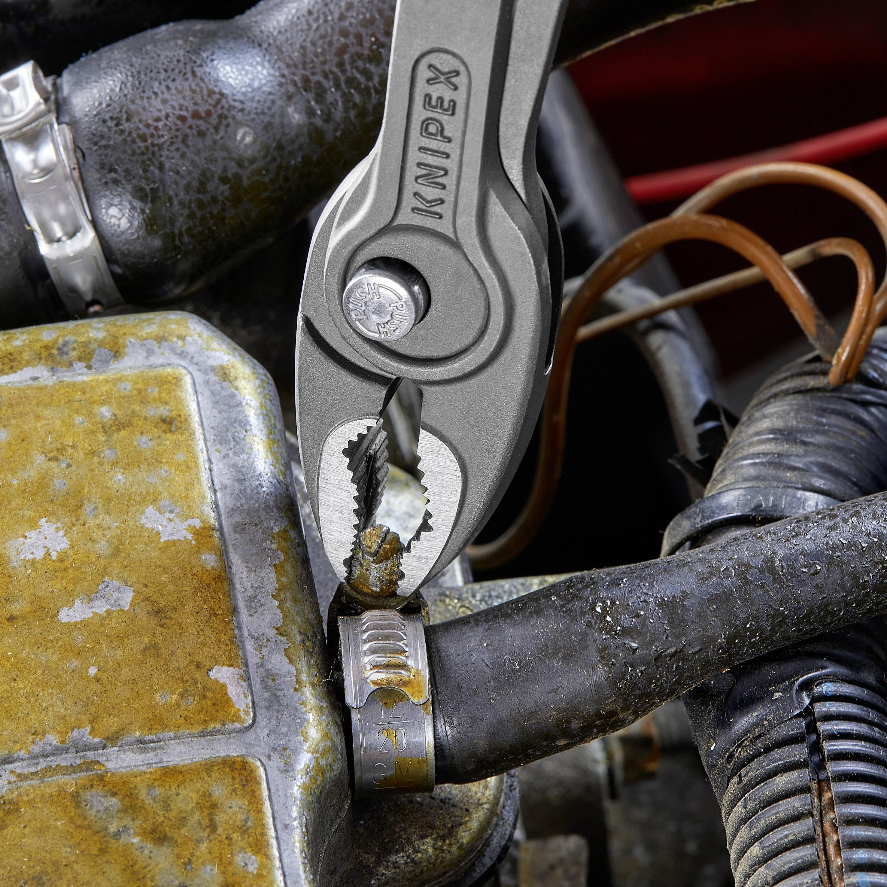 En KNIPEX-tång klipper av en rostig slangklämma på ett gammalt metallrör.