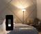 Hand håller smarttelefon med ljus lampa på skärmen, står framför upplyst golvlampa i sovrummet. Ljusstyrka: 0%-100%.
