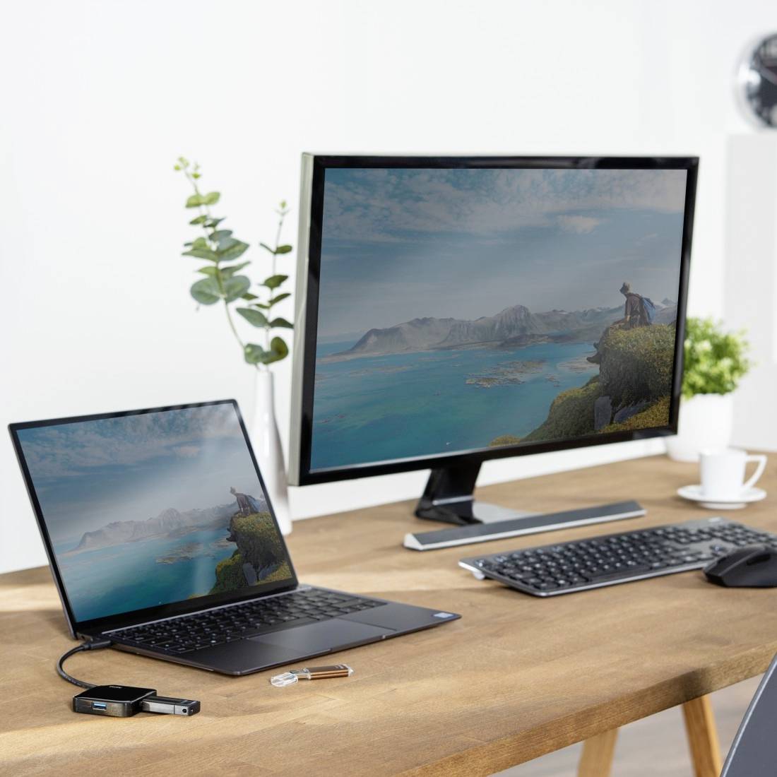 Ett skrivbord med en laptop och en stor skärm som visar samma landskapsbild. Bredvid ligger ett tangentbord och en mus.