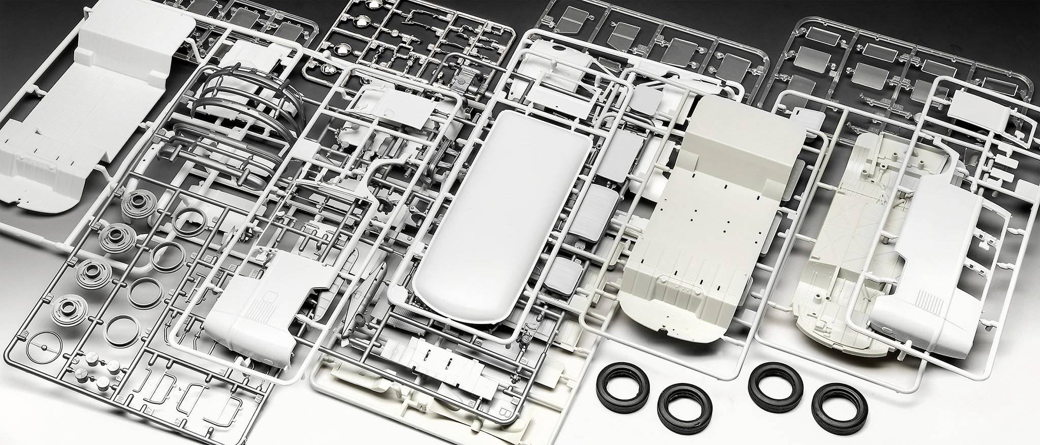 En modellbyggsats med delar av en stridsvagn är utbredd på ett bord. Olika plastdetaljer och hjul syns.