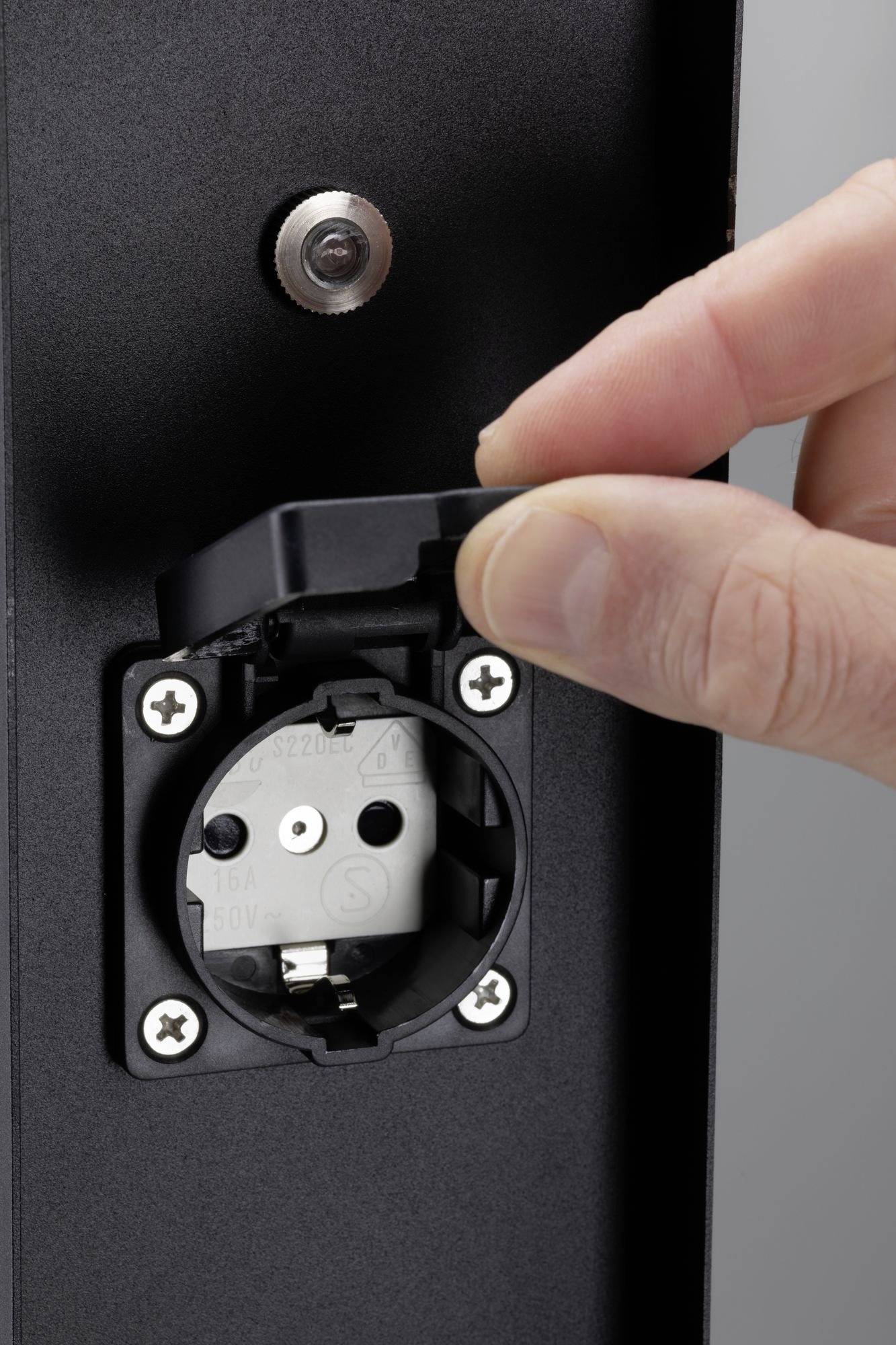 En person öppnar locket på ett svart vägguttag. Uttaget är klargjort för användning.