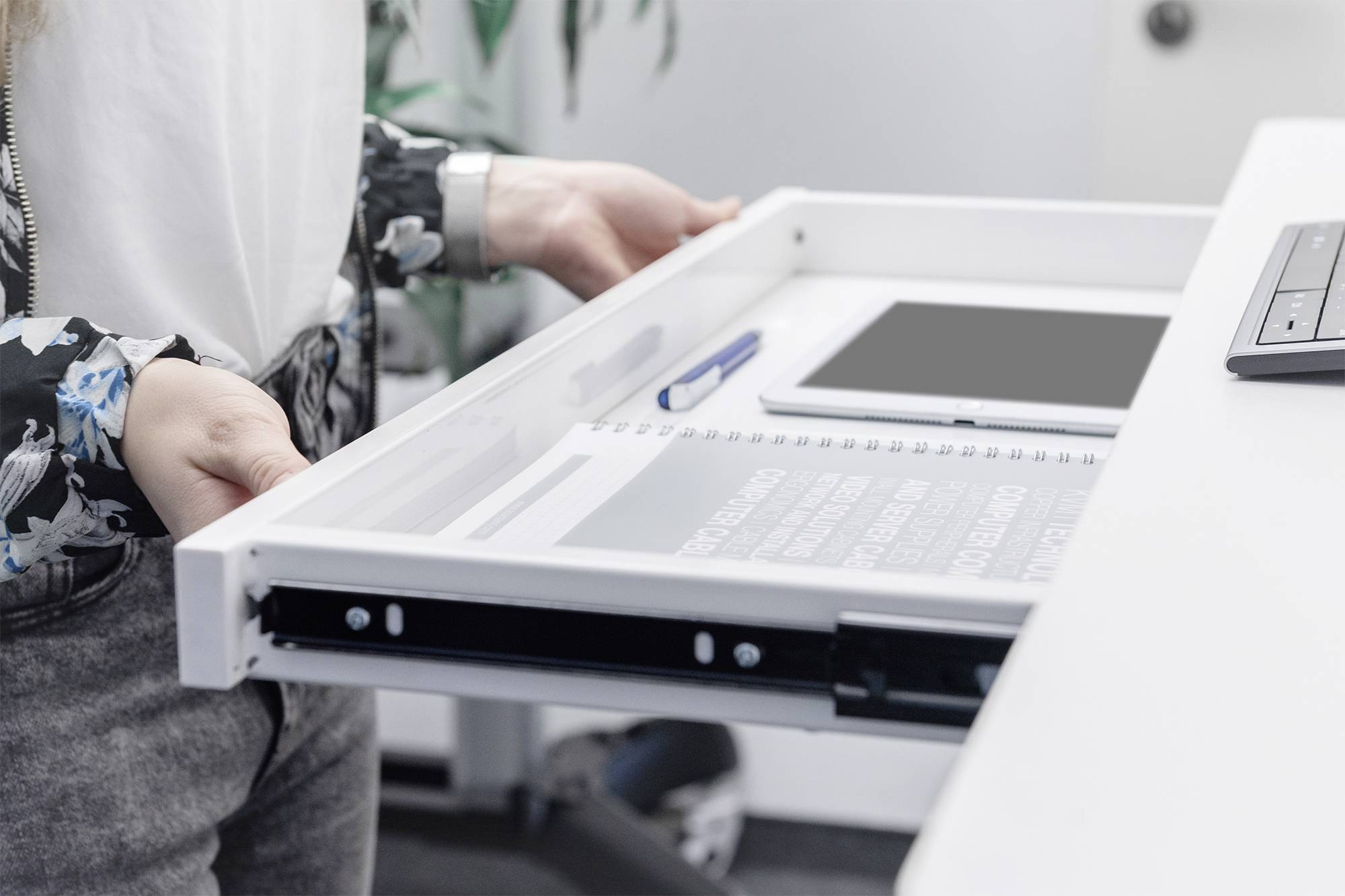 En person öppnar en vit låda i ett skrivbord. I lådan finns en anteckningsbok och en penna.