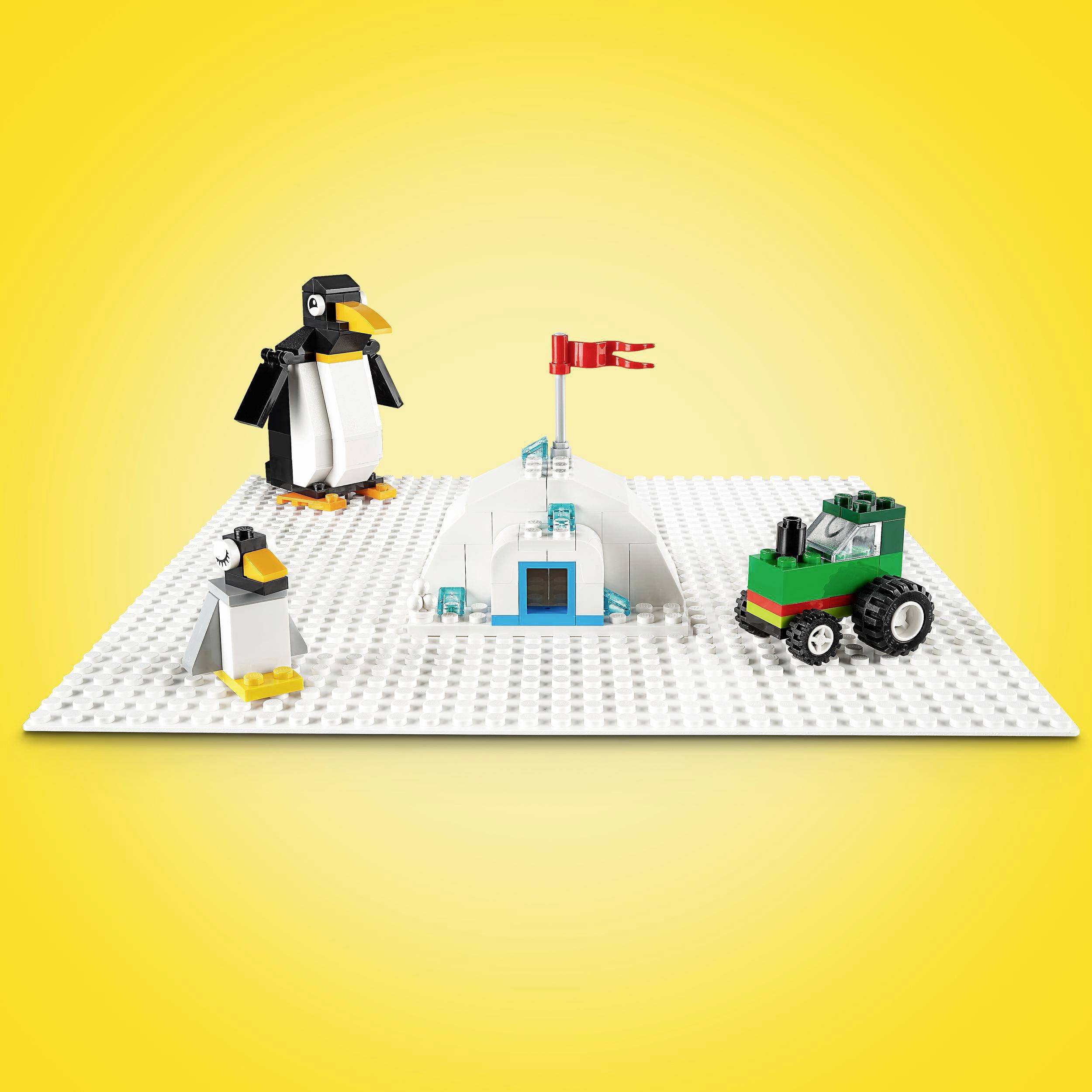 Legoscen på en vit platta: Två pinguiner, ett igloo med röd flagga och en liten grön traktor framför en gul bakgrund.