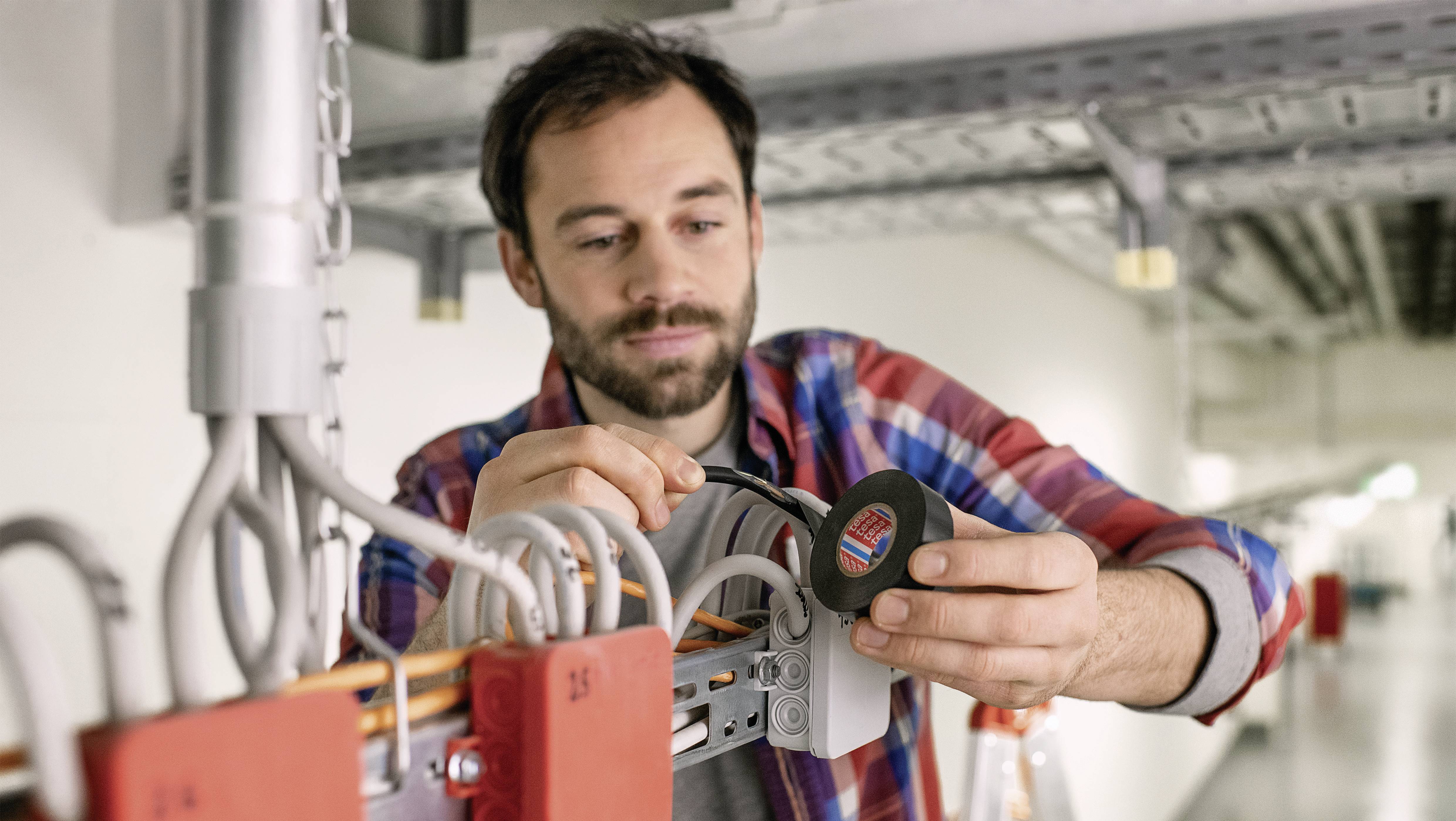 En man installerar en rund, teknisk apparat vid ett kabelsystem i en industriell inomhusmiljö.