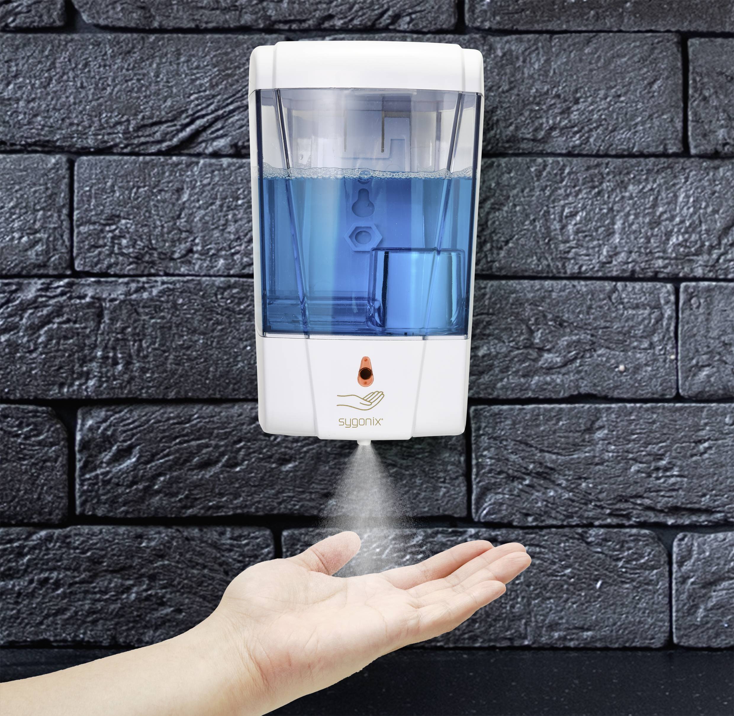 En hand använder en dispenser för att spraya blå handdesinfektionsmedel på en hand. Dispensern hänger på en svart vägg.