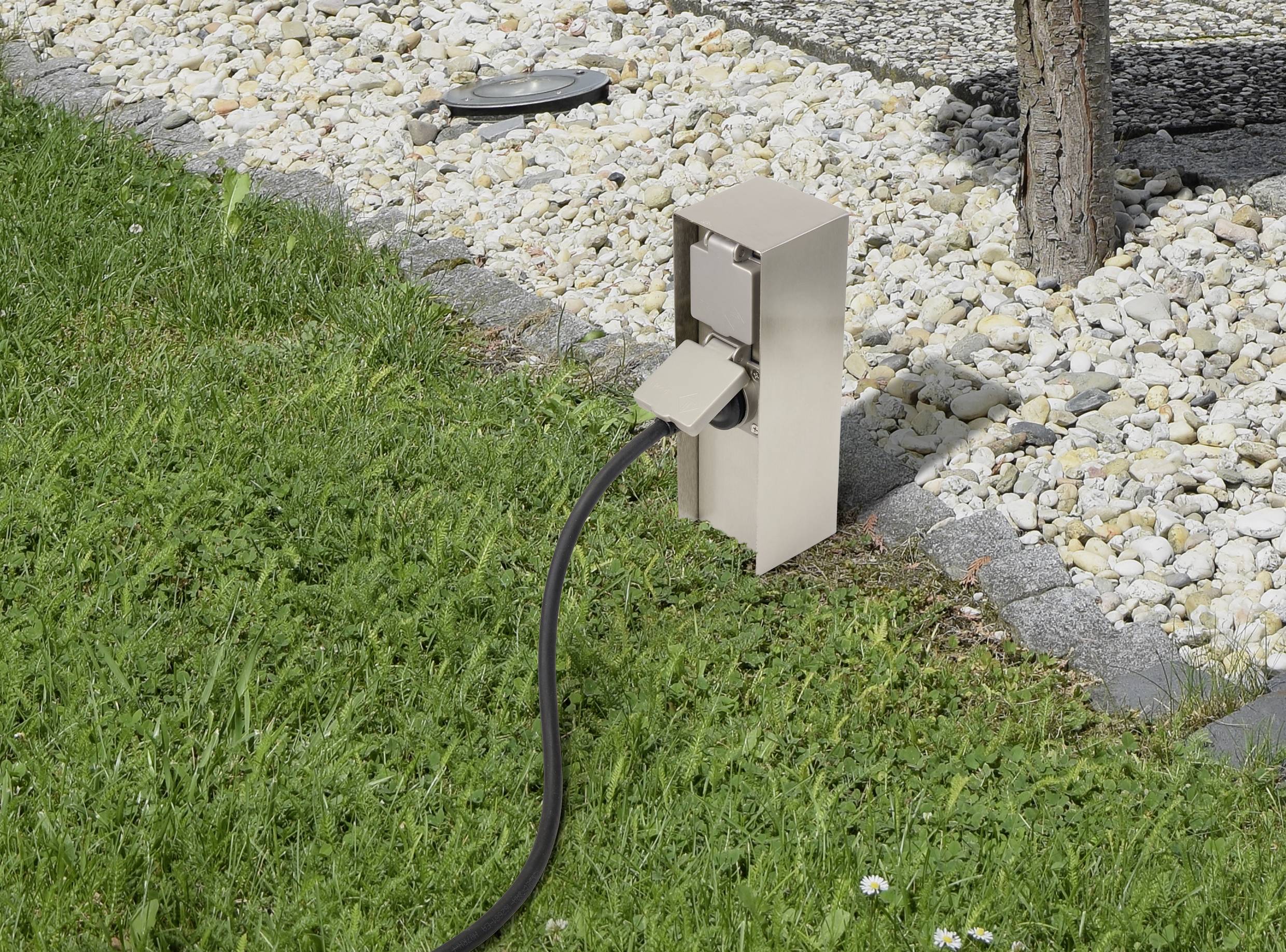 Elskåp i trädgården bredvid en grusgång, en svart kabel är inkopplad.