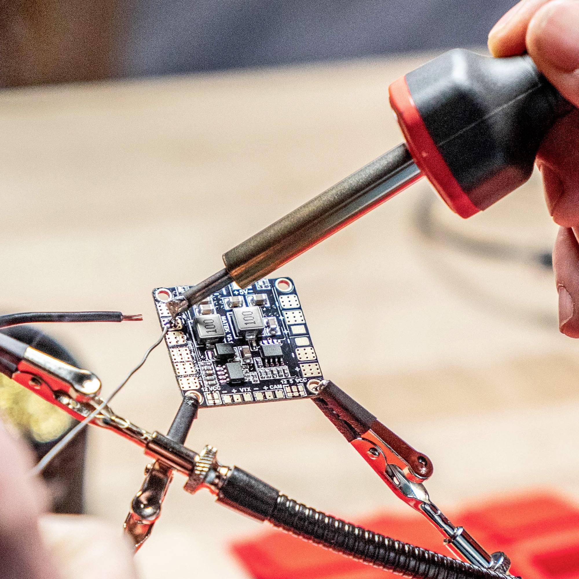 En person arbetar med en lödkolv på ett elektroniskt kretskort som innehåller flera komponenter.