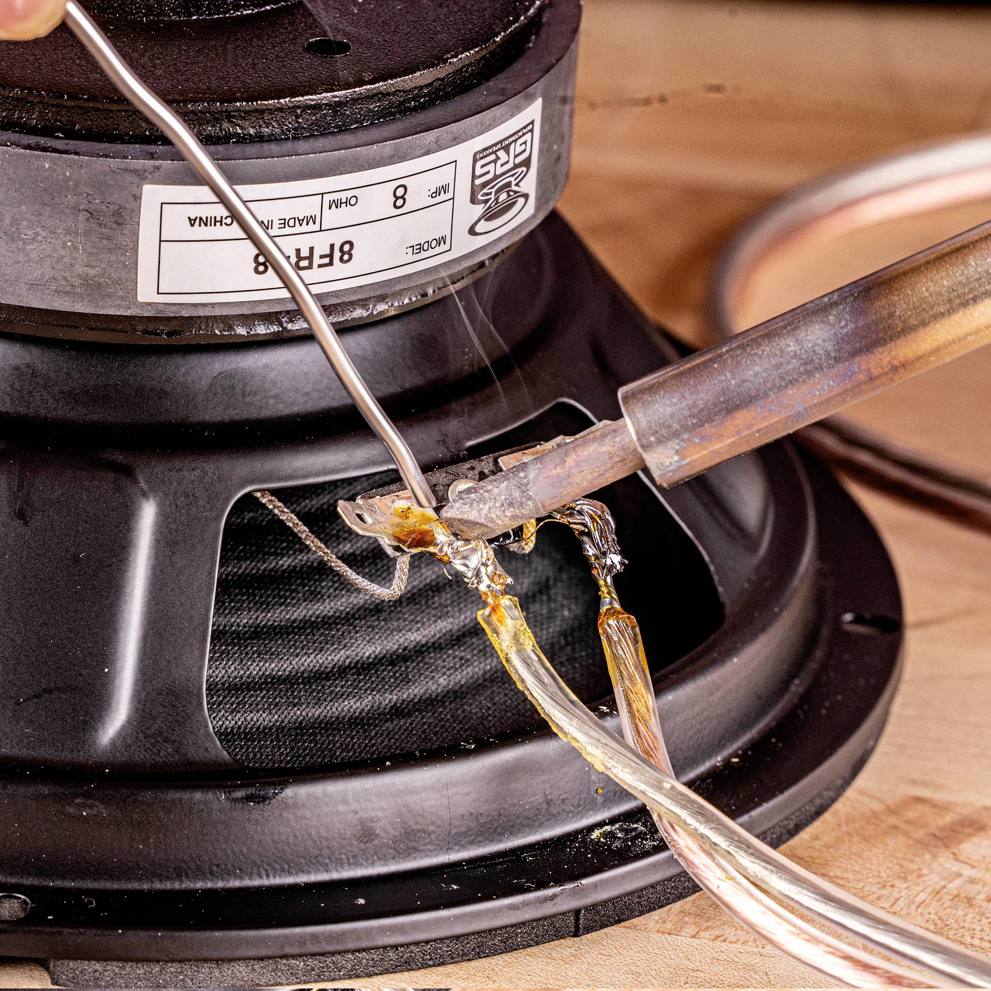 En lödspets förbinder trådar på en högtalare, vilket tyder på en reparation eller ett DIY-elektronikprojekt.