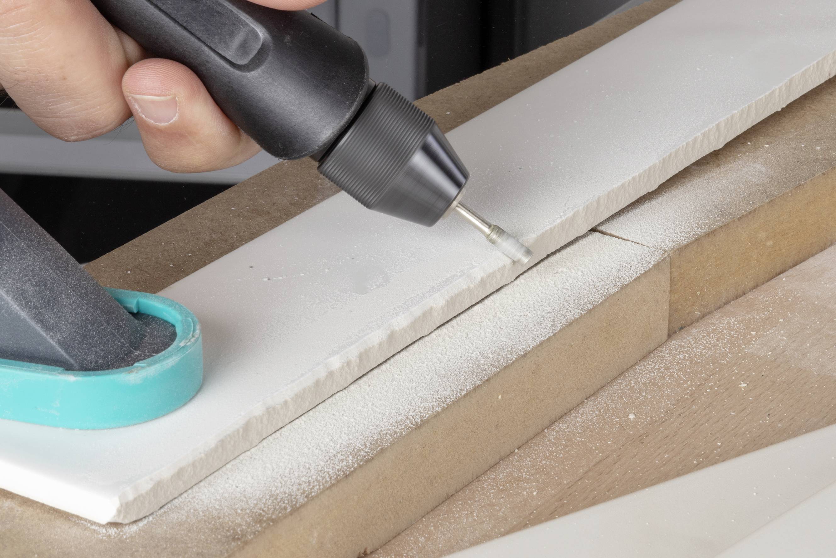 En person skär en rak linje i kakel eller stenplattor med ett roterande verktyg. Fint damm bildas under skärprocessen.