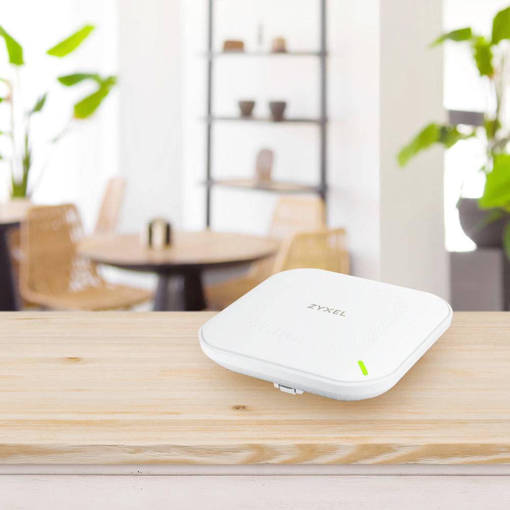 En vit WiFi-router står på ett bord i förgrunden, med ett oskarp caféinteriör med stolar och växter i bakgrunden.
