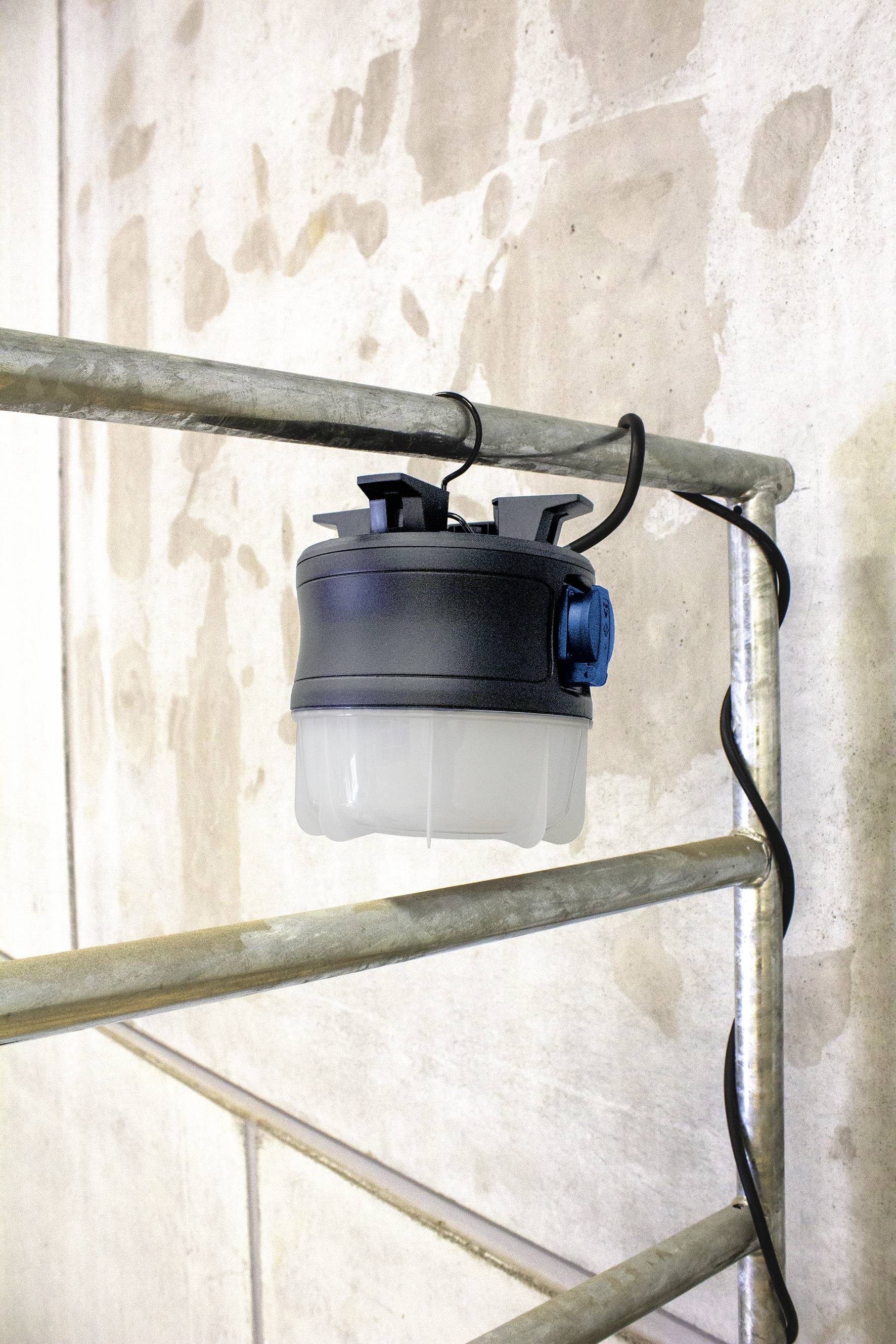En rund, bärbar lampa, fäst vid en metallställning på en betongvägg, med synlig kabel för strömförsörjning.