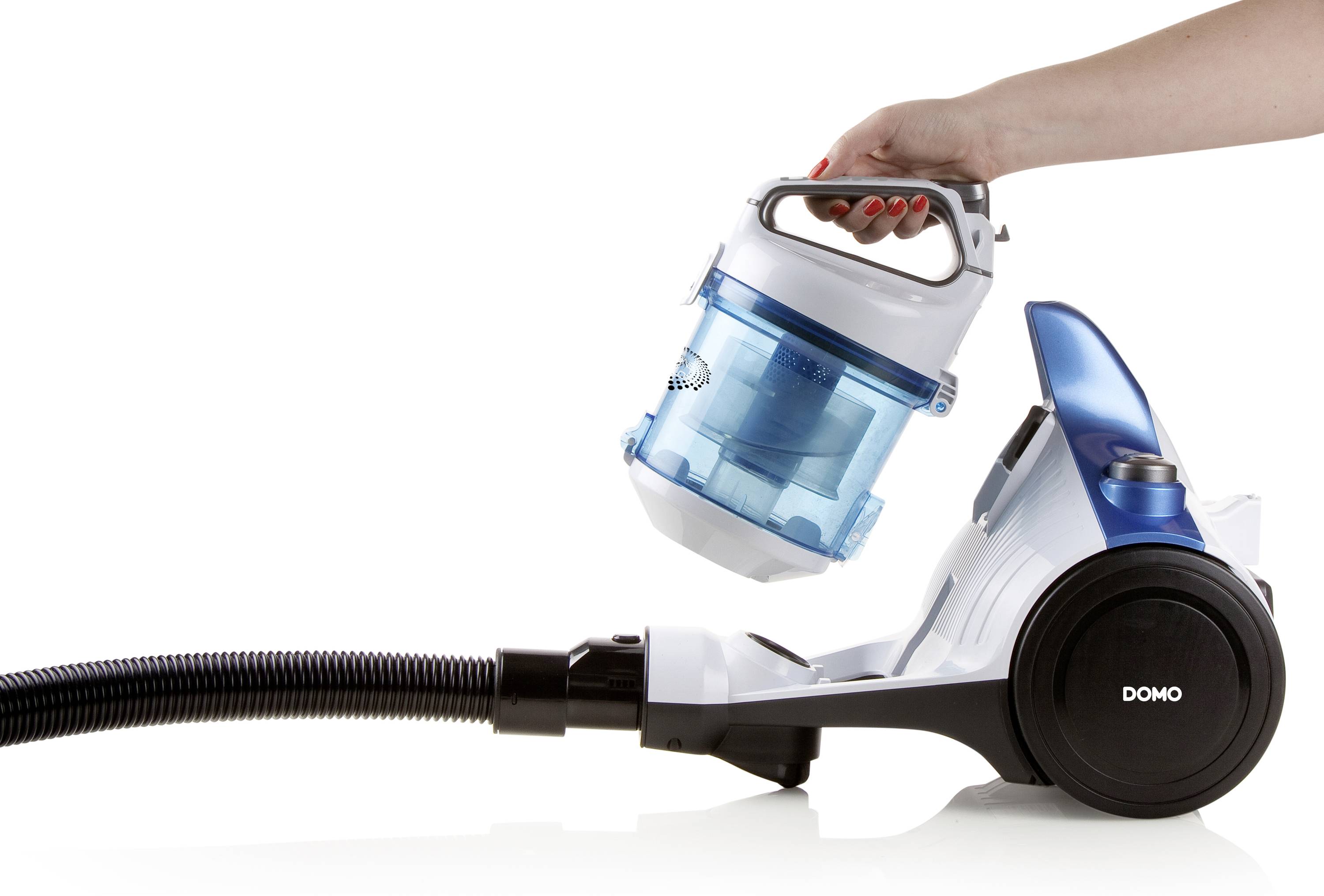 En hand lyfter upp den blå dammbehållaren från en vit dammsugare. Dammsugaren har en svart slang och hjul.