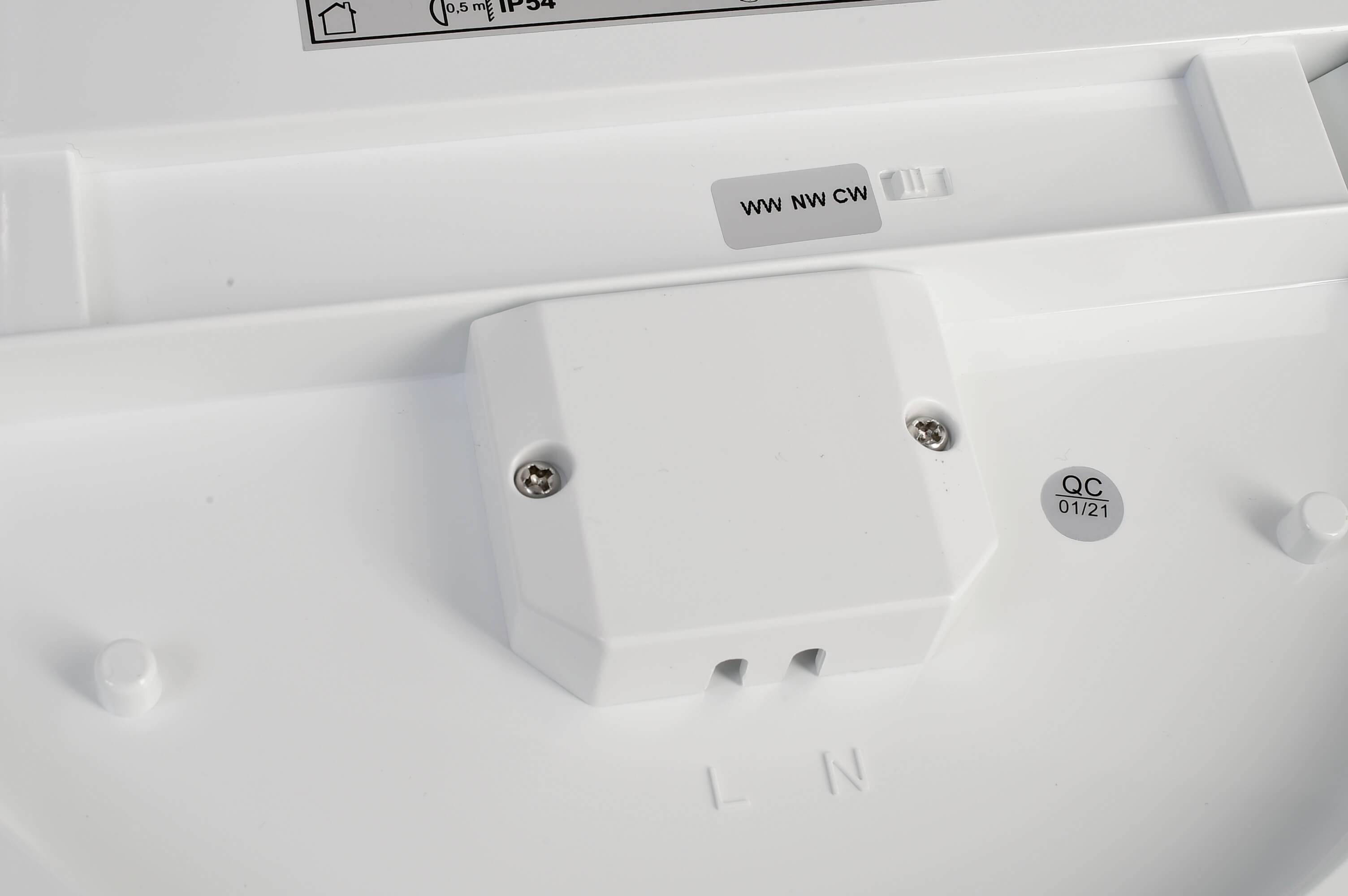 Vit plastskydd med skruvar, med klistermärken 'ww nw cw' och 'QC 01/21'. Enkel industriell design.