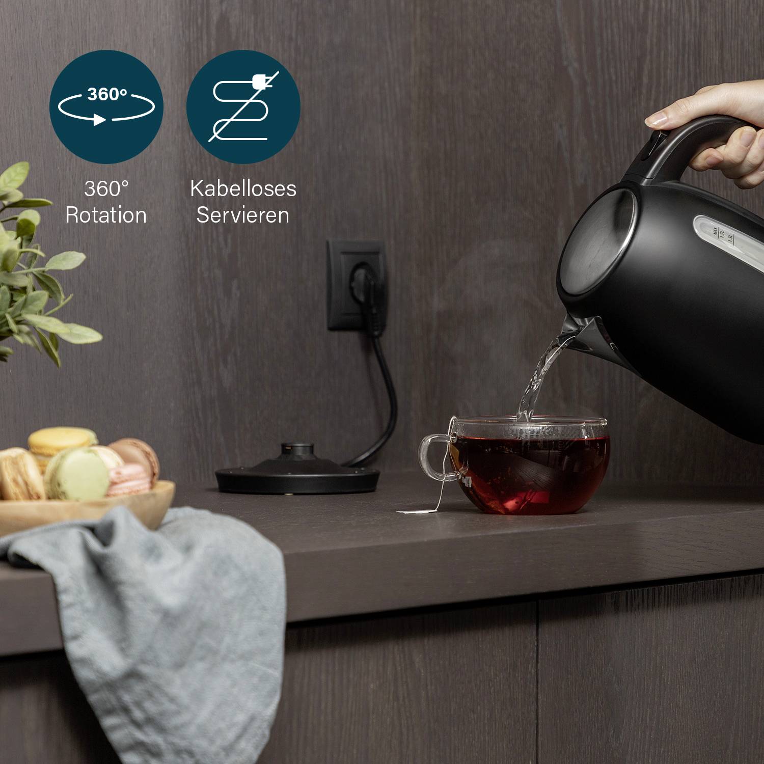Vattenkokaren fyller en kopp med te. Etiketten visar 360° rotation och sladdlös servering. Frukt och bröd på bänkskivan.