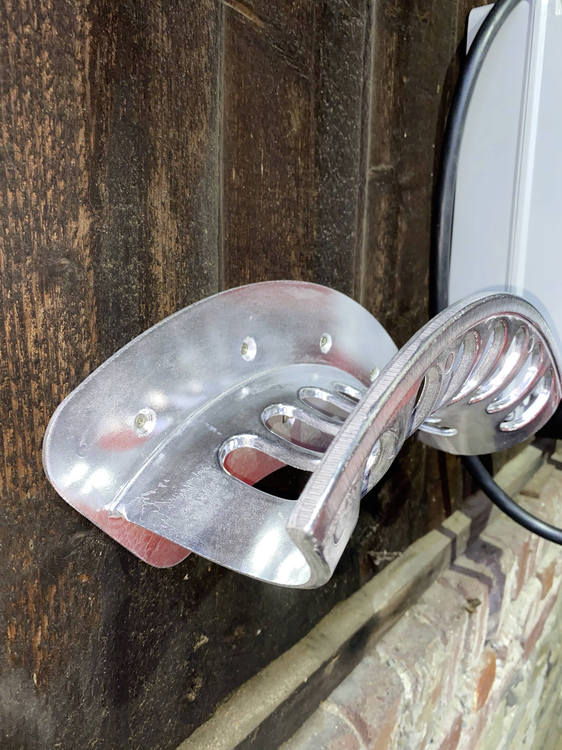 Metallhållare monterad på en trävägg, troligen avsedd för att hänga upp en cykel, kablar i närheten.