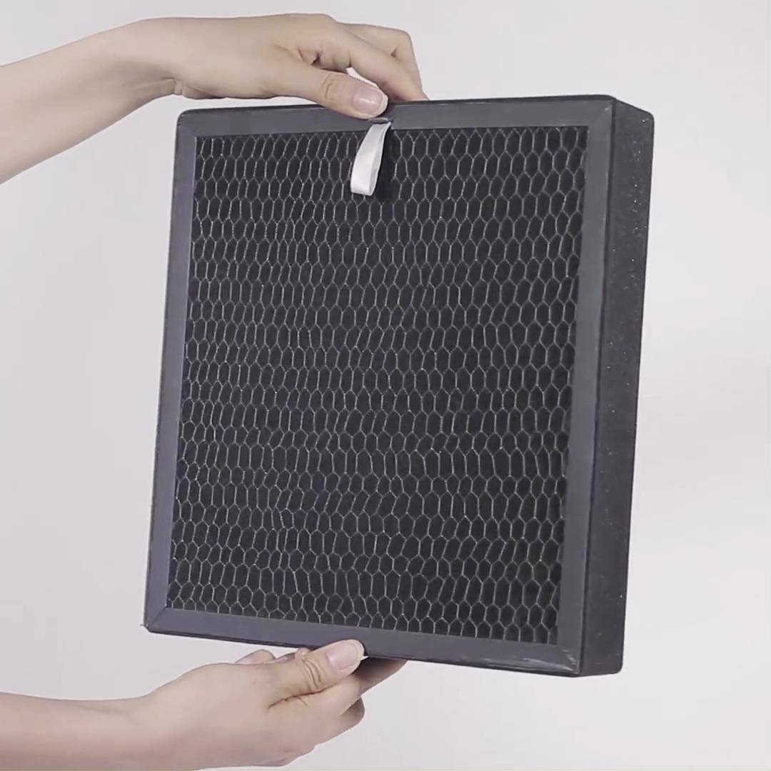 En person håller ett fyrkantig luftfilter med svart honeycomb-nät.