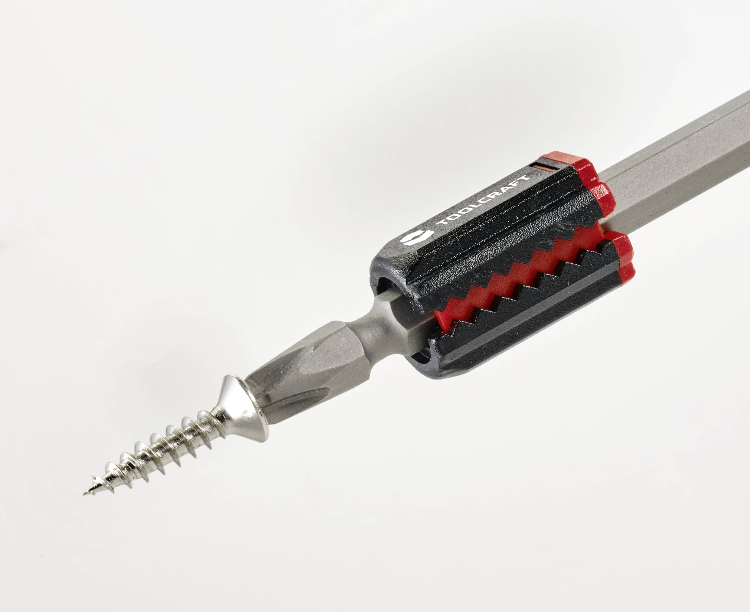 Närbild av en skruvmejsel med monterad skruv, fastsatt i en magnetisk bitshållare med grått handtag och röda detaljer.